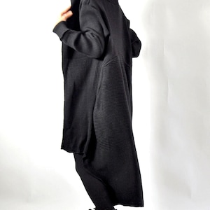 A profile view of a person wearing a long black hooded knit cardigan and white boots.