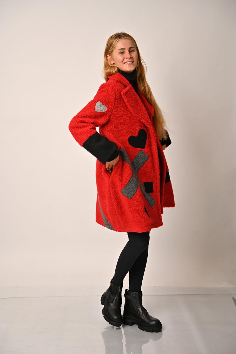 May include: A red fleece coat with black and grey patches in the shape of hearts and an X. The coat has a collar and long sleeves.