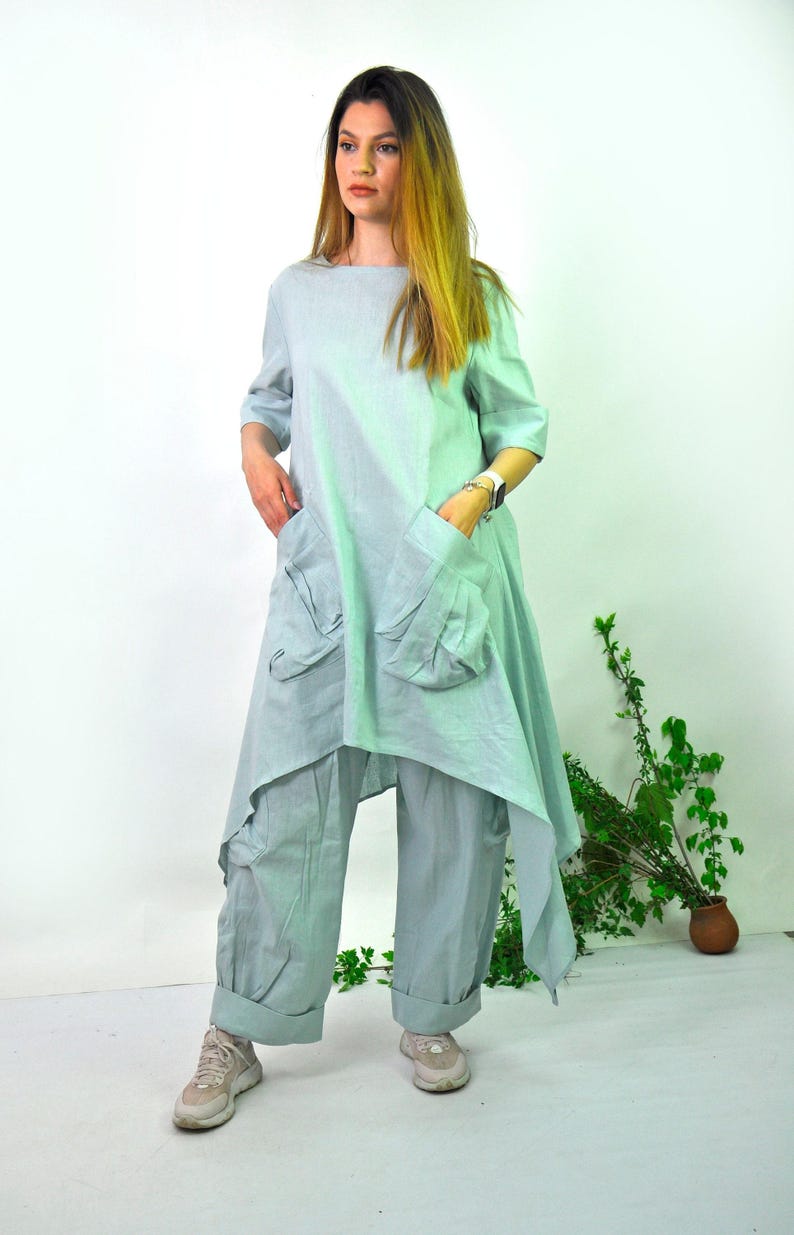 A woman in a light green linen tunic with large pockets and cargo pants set, with sneakers, stands with hands in her pockets.