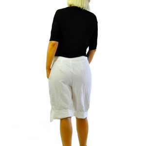 May include: A black short-sleeved top and white shorts are worn with black platform sandals. The shorts have a cuffed hem and a side detail. The person is facing away from the camera against a white background.