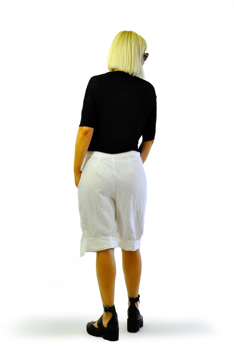 May include: A black short-sleeved top and white shorts are worn with black platform sandals. The shorts have a cuffed hem and a side detail. The person is facing away from the camera against a white background.