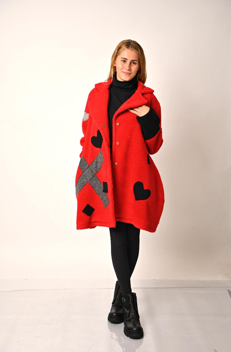 May include: A red fleece coat with black heart and grey geometric designs. The coat has a button closure and a collar.