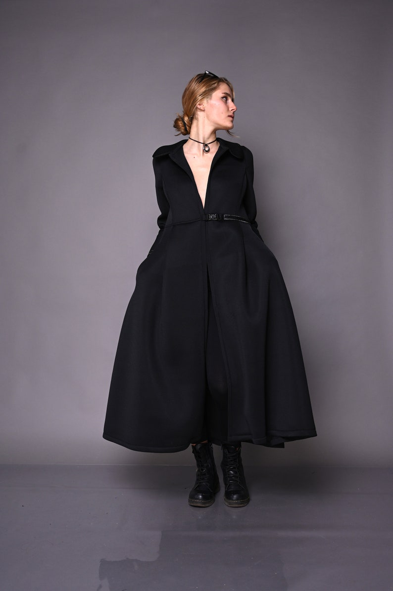May include: A black long-sleeved coat with a V-neckline and a belt. The coat has a flared skirt and is worn with black boots.