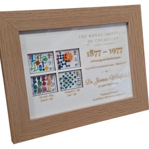 May include: A framed print with commemorative stamps and text from The Royal Institute of Chemistry, celebrating 100 years from 1877-1977. The frame is made of light brown wood. The print includes the name "Dr. James Whitfield".