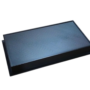 Puede incluir: Una caja rectangular negra con una tapa azul oscuro texturizada. La caja tiene un perfil bajo y un diseño simple y elegante. La superficie de la tapa tiene un sutil patrón de trama cruzada. La caja está sobre un fondo blanco.