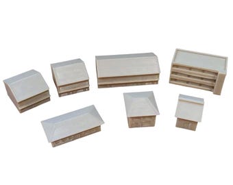 May include: A collection of seven miniature building models in a light beige color. The set includes various structures with sloped roofs, rectangular footprints, and textured surfaces, all rendered in a uniform, unpainted resin material.