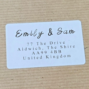 Peut inclure: Étiquette d'adresse blanche avec du texte noir. Le texte indique "Emily & Sam", "77 The Drive", "Aldwich, The Shire", "AA99 4BB", et "United Kingdom".