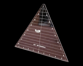 May include: A clear acrylic 60-degree triangle quilting ruler featuring black printed measurement markings and grid lines. The tool displays the text EmiB Designs and 8 1/2 inch 60 degree triangle, with numbered increments along the edges and center.