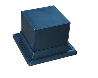 May include: A dark blue, square pedestal with a matching square base. The pedestal is a cube shape, and the base has a slightly curved edge. The surface has a textured appearance.