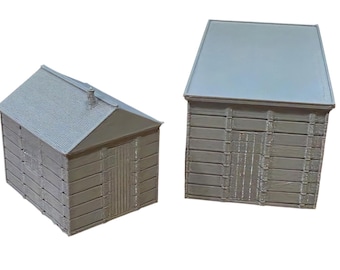 May include: Two miniature gray structures with a plank-style exterior texture. One model features a peaked roof with a small chimney detail, while the other has a flat, rectangular roof. Both models display vertical door panels and horizontal siding.