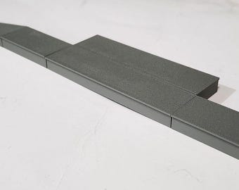 May include: A set of dark gray modular ramp components with a textured, non-slip surface. The pieces include flat rectangular platforms and sloped sections that connect to form a continuous, low-profile incline path for small wheeled items.