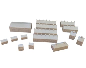 May include: A collection of unpainted off-white miniature building models for tabletop gaming. The set includes various rectangular structures, including long row houses, smaller detached buildings, and a large warehouse-style building.
