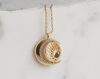 May include: A gold necklace with a crescent moon pendant featuring a sunburst design and a small diamond in the center.