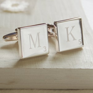 May include: Silver cufflinks with square engraved plates. The left cufflink has the letter "M" engraved on it with the number "3" below it. The right cufflink has the letter "K" engraved on it with the number "5" below it.