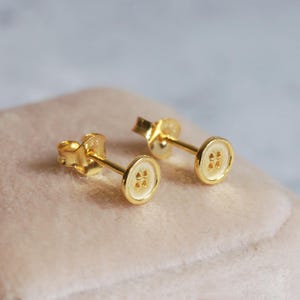 Puede incluir: Un par de pendientes de botón de oro. Los pendientes son pequeños y tienen un diseño sencillo.