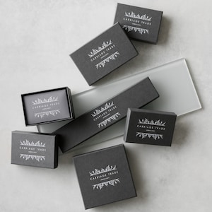 May include: Multiple black boxes with the text "Carriage Trade Jewellery" in white lettering. The boxes are arranged on a light gray surface.