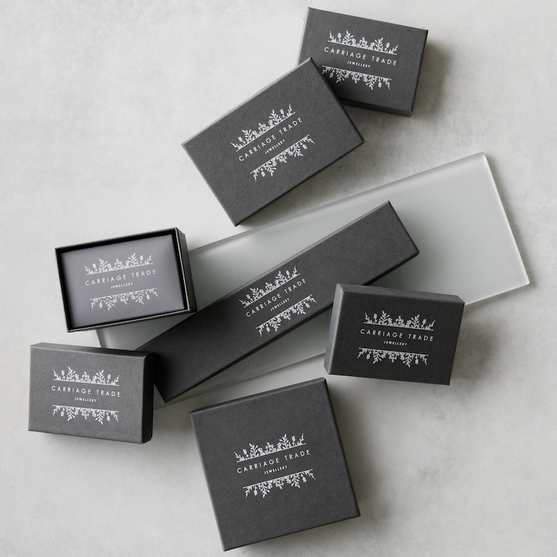 May include: Multiple black boxes with the text "Carriage Trade Jewellery" in white lettering. The boxes are arranged on a light gray surface.