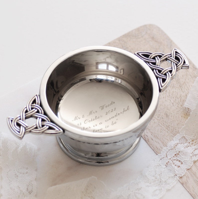 Pode incluir: Uma tigela prateada com al&ccedil;as de n&oacute;s celtas. A tigela tem uma borda larga e uma base de pedestal. No interior est&aacute; gravado: "Mr & Mrs Woods 13 October 2022 there is a wonderful lace to be."