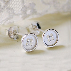 May include: A pair of silver button stud earrings. Each earring features a small, round button with four holes.
