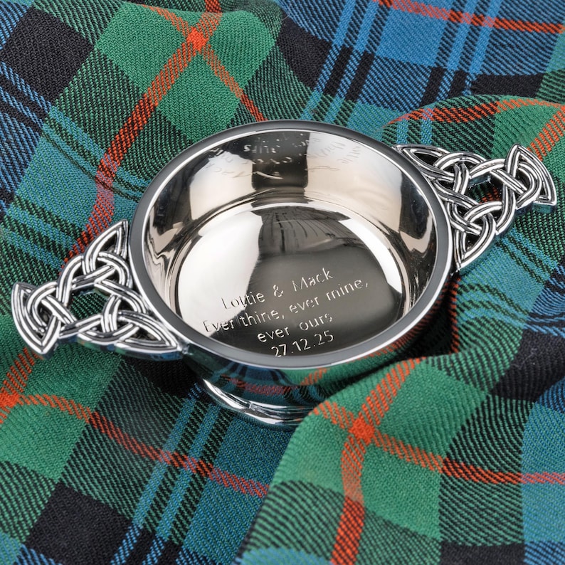 Pode incluir: Uma tigela prateada com al&ccedil;as de n&oacute;s celtas. A tigela tem uma inscri&ccedil;&atilde;o gravada: "Lottie & Mack, Ever thine, ever mine, ever ours, 27.12.25." Est&aacute; sobre um tecido xadrez verde, azul e vermelho.