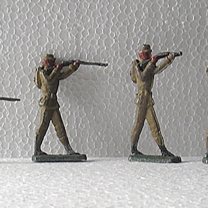 May include: A set of vintage toy soldiers in khaki uniforms, each holding a rifle. The figures have red details and are posed in different positions, including kneeling and standing, ready to fire their weapons.