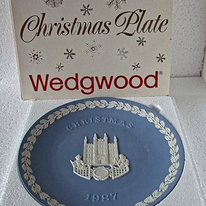 May include: A Wedgwood Christmas plate featuring a blue and white design of the Houses of Parliament with a holly border and the year 1987.