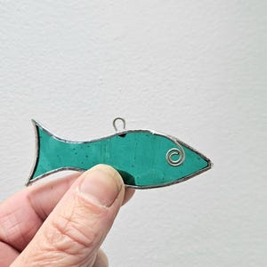 Pu&ograve; includere: Un ornamento a forma di pesce in vetro colorato turchese con un contorno in filo d'argento. Il pesce ha un filo ad anello nella parte superiore per appenderlo. L'occhio del pesce &egrave; una piccola spirale argentata.