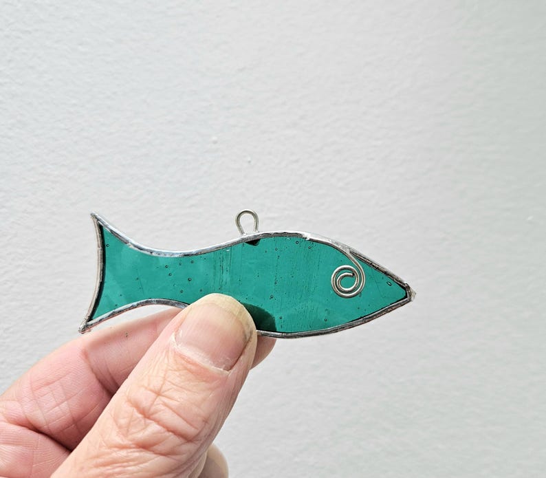 Pu&ograve; includere: Un ornamento a forma di pesce in vetro colorato turchese con un contorno in filo d'argento. Il pesce ha un filo ad anello nella parte superiore per appenderlo. L'occhio del pesce &egrave; una piccola spirale argentata.