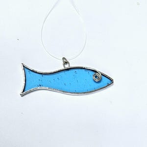 Pu&ograve; includere: Ciondolo a forma di pesce in vetro colorato, con corpo azzurro chiaro e contorno in metallo argentato. Il pesce ha un occhio a spirale ed &egrave; sospeso da un cordino trasparente. Il ciondolo misura circa 7.6 cm di lunghezza.