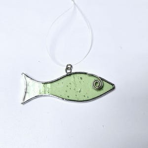 Pu&ograve; includere: Un ornamento a forma di pesce in vetro colorato verde chiaro, con un contorno in metallo color argento e un dettaglio a spirale in filo di ferro. Il pesce &egrave; sospeso da un filo trasparente, adatto per essere appeso. Un oggetto decorativo.