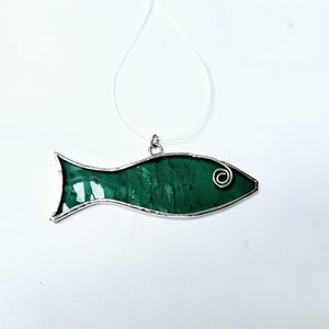 Pu&ograve; includere: Ciondolo a forma di pesce in vetro colorato verde, realizzato a mano, con una cornice in metallo color argento e un ricciolo decorativo sulla testa. Il ciondolo &egrave; appeso a un cordino sottile e trasparente, perfetto per una collana.