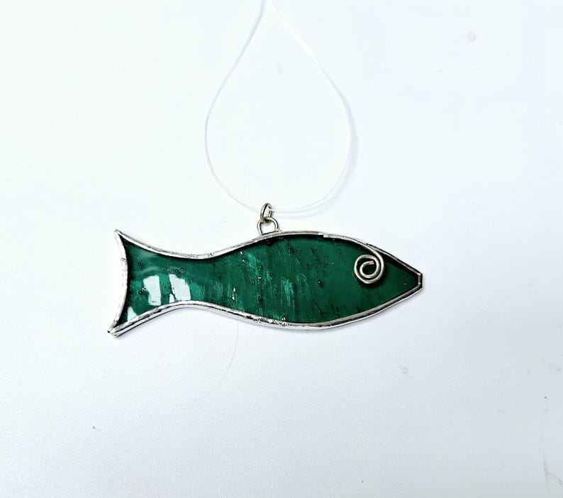 Pu&ograve; includere: Ciondolo a forma di pesce in vetro colorato verde, realizzato a mano, con una cornice in metallo color argento e un ricciolo decorativo sulla testa. Il ciondolo &egrave; appeso a un cordino sottile e trasparente, perfetto per una collana.