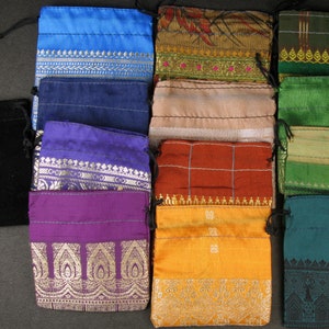Op de afbeelding: Assortiment van 12 kleine trekkoordzakjes in verschillende kleuren en patronen. De zakjes zijn gemaakt van verschillende stoffen, waaronder fluweel, zijde en katoen. Sommige zakjes hebben geborduurde ontwerpen, terwijl andere bedrukte patronen hebben.
