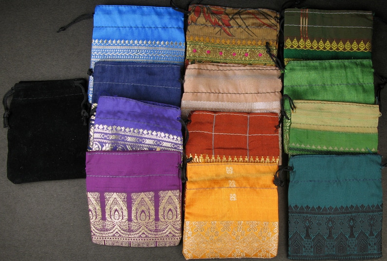 Op de afbeelding: Assortiment van 12 kleine trekkoordzakjes in verschillende kleuren en patronen. De zakjes zijn gemaakt van verschillende stoffen, waaronder fluweel, zijde en katoen. Sommige zakjes hebben geborduurde ontwerpen, terwijl andere bedrukte patronen hebben.
