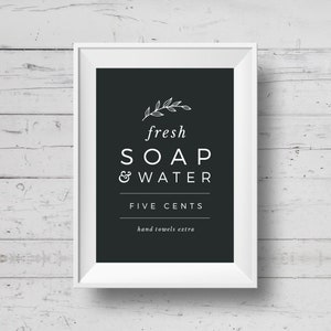 May include: A white framed sign with black background and white text that reads "fresh SOAP & WATER FIVE CENTS hand towels extra". The sign has a small leaf design at the top.