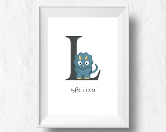 May include: A white framed print with a black letter L and a blue dinosaur inside the letter. The text "L is for LIAM" is below the letter.