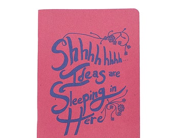May include: A rectangular, pink notebook with the words "Shhhhh... Ideas are Sleeping in Here" in blue script. The notebook has a simple, clean design, perfect for jotting down thoughts and ideas.