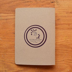 May include: A brown paper notebook with a purple circle logo that says "100% Recycled Content Made in the USA 37 Pages".
