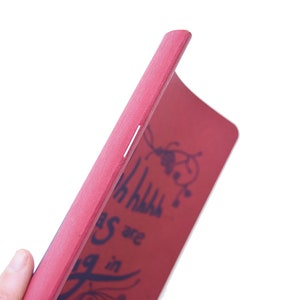 Puede incluir: Un libro de madera rojo con las palabras "Things are going in" y un dise&ntilde;o floral decorativo en azul oscuro. El borde del libro es visible, mostrando una franja de color claro. El libro se sostiene en &aacute;ngulo.