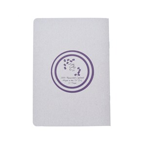 May include: A white notebook with a purple circle logo that says "The Ugly  Grocery Co.". The circle also says "100% Recycled Content, Made in the U.S.A., 32  Pages".