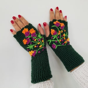 May include: A pair of green fingerless gloves with colorful embroidered flowers. The gloves are crocheted and have a scalloped edge.