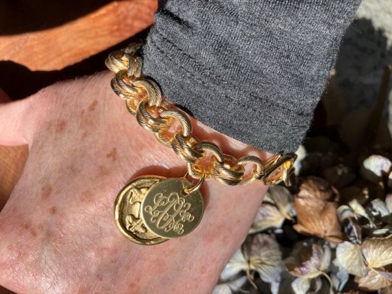 May include: A gold chain bracelet with a large, round charm featuring the initials "L.L." in a cursive font.