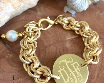 May include: A gold-toned chain link bracelet featuring a circular pendant engraved with the monogram letters DJF. The bracelet includes a lobster claw clasp and a single white pearl charm attached near the closure, showcasing a textured finish.