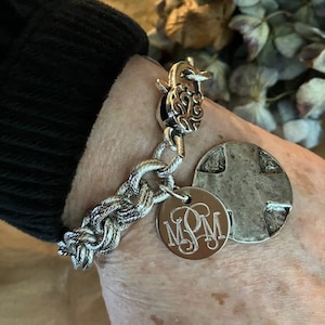 May include: A silver chain bracelet with a silver charm that says "MSM" and a silver cross charm. The bracelet is on a person's wrist.