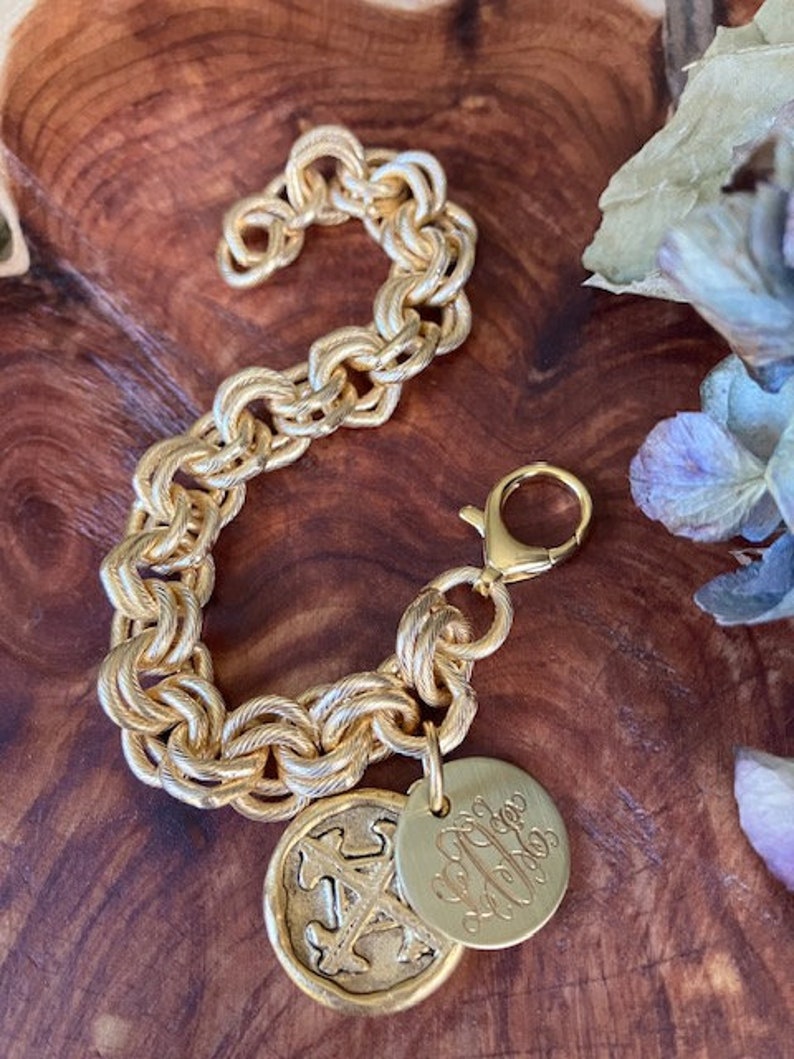 May include: A gold chain bracelet with a gold charm featuring a monogram and a gold charm with a textured design.