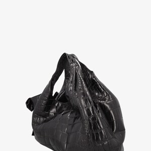 May include: A black, textured handbag with a crocodile-like pattern. The bag has a soft, slouchy shape with a single handle. The material appears to be leather or a leather-like material. The bag is set against a white background.