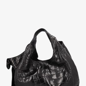May include: A black leather hobo bag with a crocodile skin texture. The bag has a single shoulder strap and a large, open interior. The bag is made of a shiny, textured leather and has a slouchy shape. The bag is a dark, solid black color.