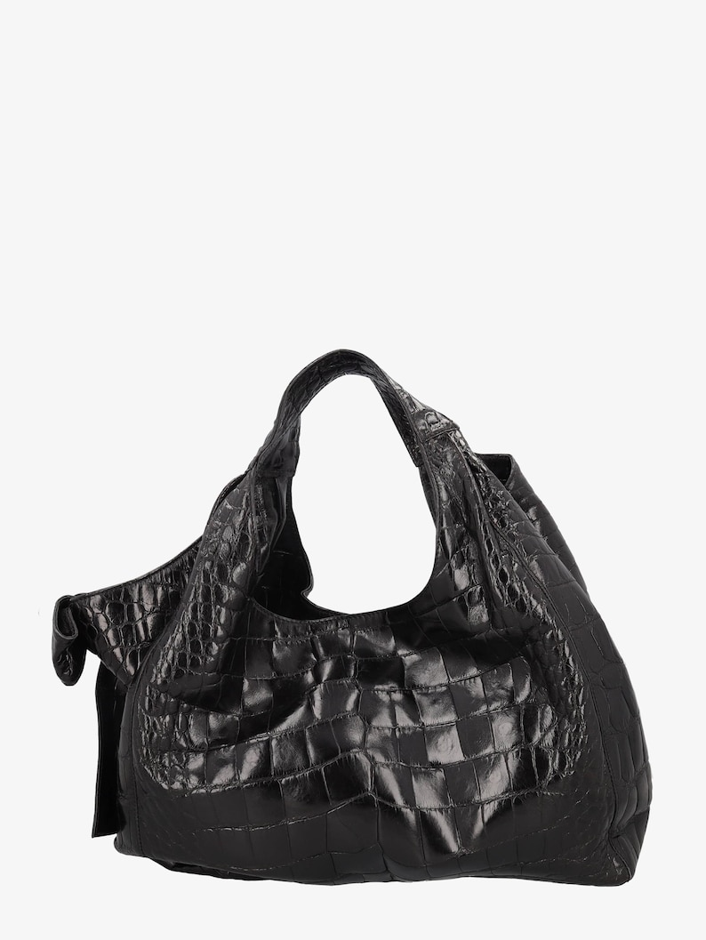 May include: A black leather hobo bag with a crocodile skin texture. The bag has a single shoulder strap and a large, open interior. The bag is made of a shiny, textured leather and has a slouchy shape. The bag is a dark, solid black color.