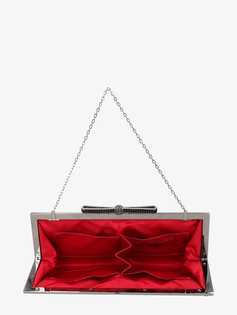 Pode incluir: Embreagem prateada aberta com interior de cetim vermelho. A embreagem apresenta um la&ccedil;o decorativo com enfeites pretos e prateados e uma al&ccedil;a de corrente prateada. O interior tem v&aacute;rios bolsos.