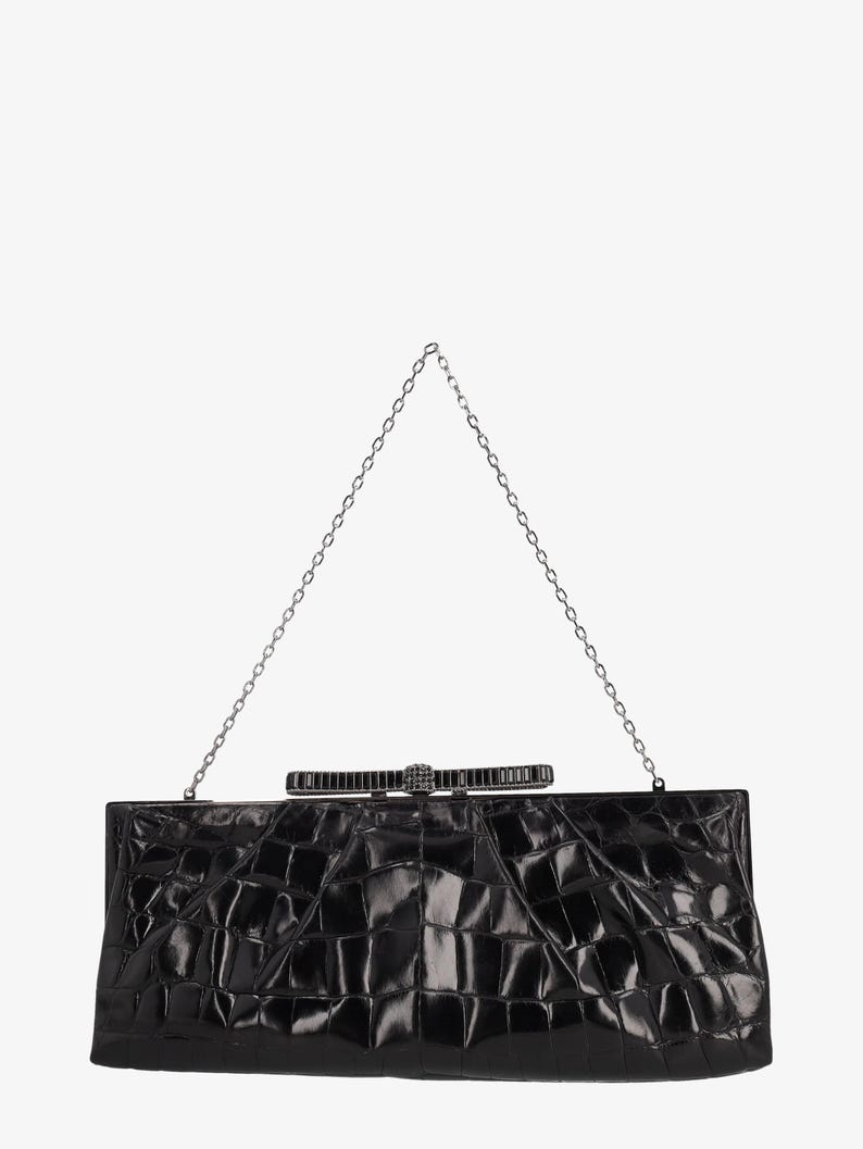 Pode incluir: Uma clutch retangular preta com um padr&atilde;o texturizado semelhante ao de crocodilo. Possui uma corrente prateada e um fecho decorativo com design de la&ccedil;o. Um acess&oacute;rio formal.